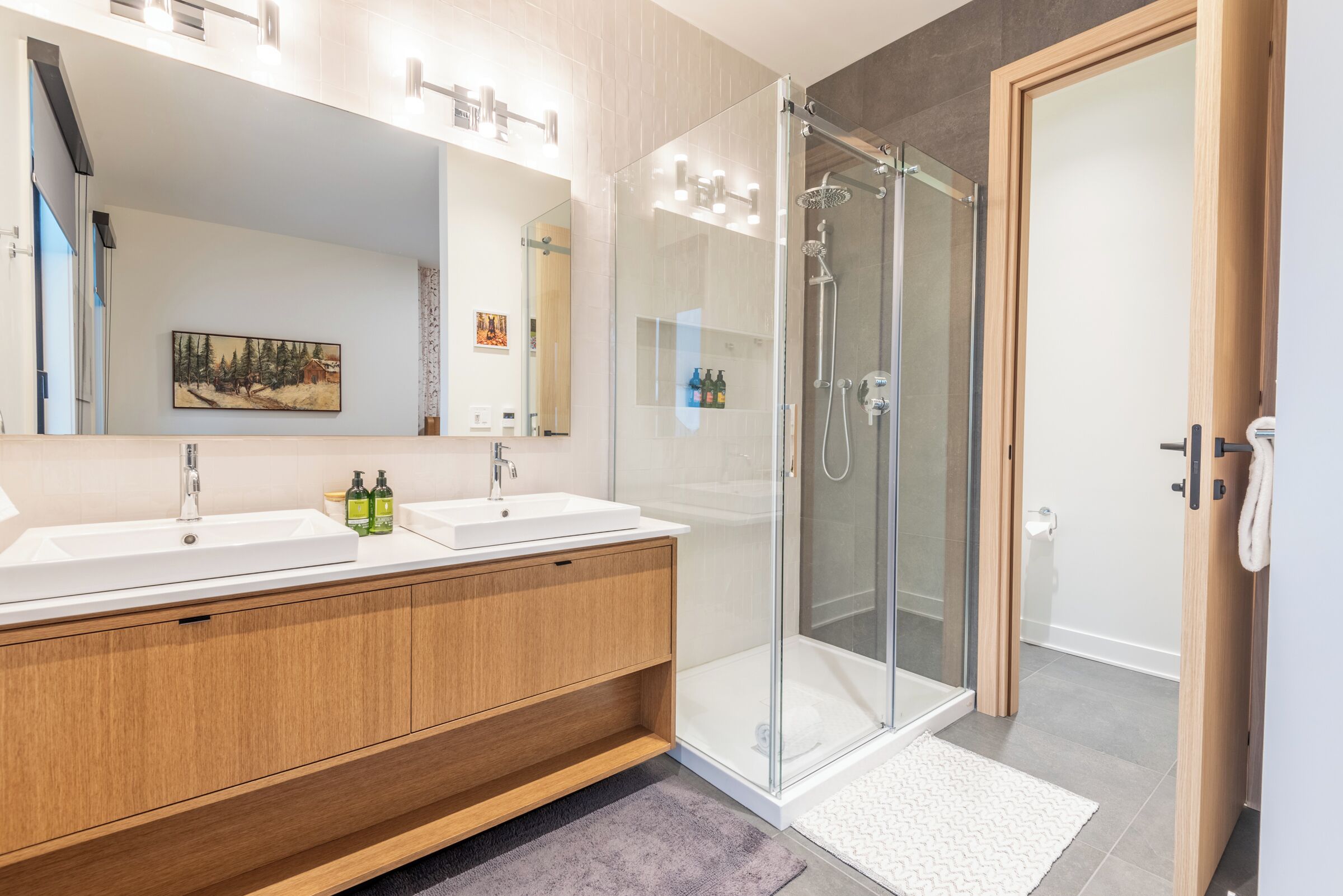 A modern bathroom with two sinks, a glass shower enclosure, and a wooden vanity.
