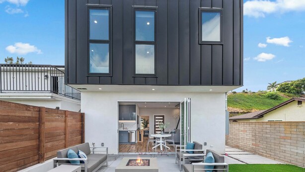 Una casa moderna de dos pisos con techo plano, ventanas amplias y un patio con muebles de exterior.