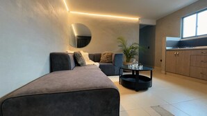 Un salon moderne comprenant un canapé, une table basse et un coin cuisine avec des placards et une fenêtre.