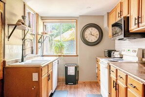 A kitchen with wooden cabinets, a sink, a stove, a microwave, and a clock on the wall.
