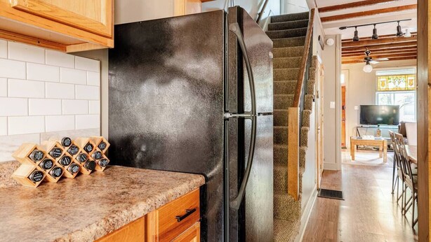 A kitchen with a black refrigerator, wooden cabinets, and a spice rack.
