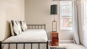 A bedroom with a bed, a nightstand, a lamp, and a window with curtains.