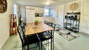 A compact kitchen with white cabinets, a wooden dining table, and a clock on the wall.