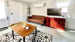 A room with a wooden table, a brown sofa, a red cabinet with a TV, and a patterned rug.