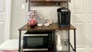 A kitchen area with a wooden clock, a coffee maker, a microwave, and a shelf with glasses and a plant.