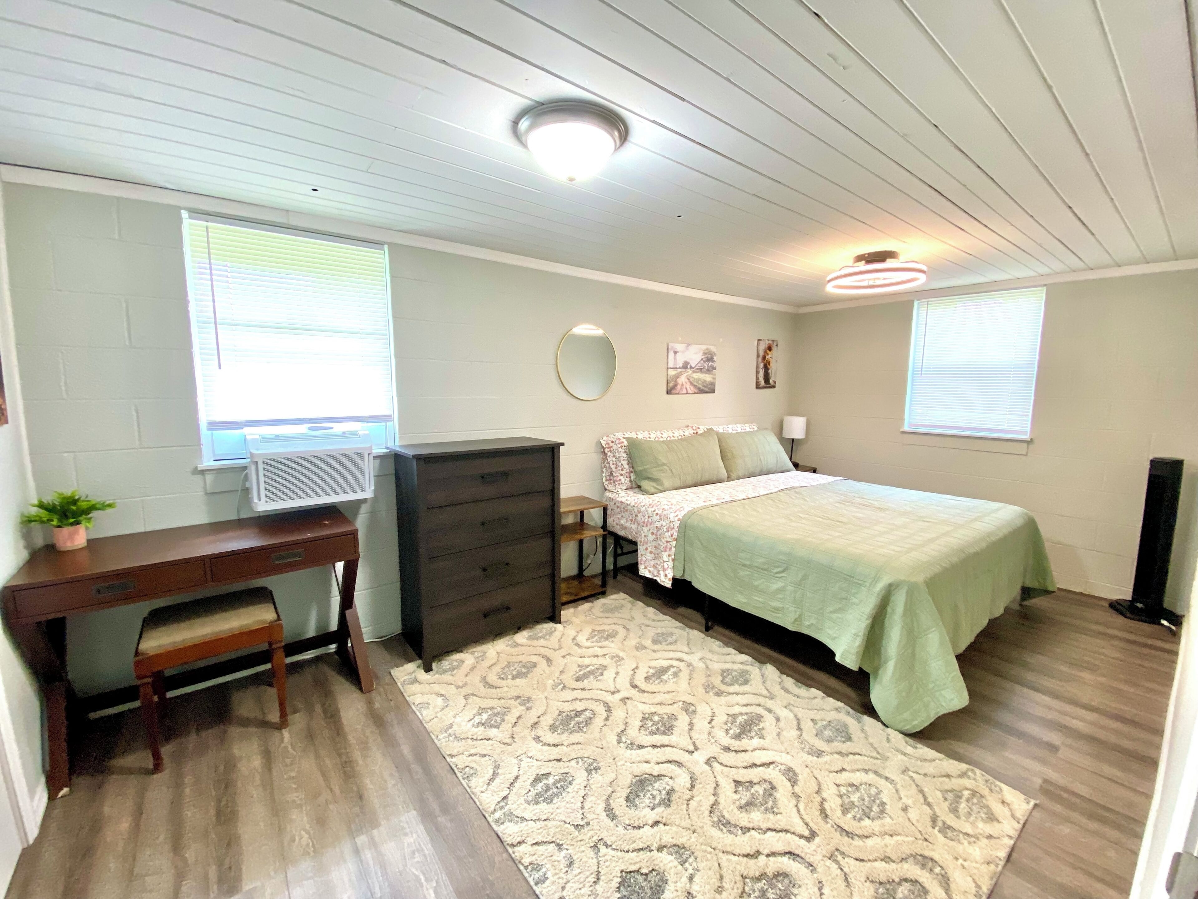 A bedroom with a bed, a desk, a dresser, and a radiator.