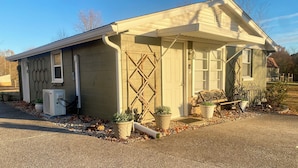A small, single-story building with a beige exterior, a front porch with a bench, and potted plants.