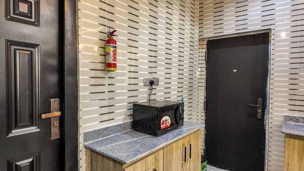 A kitchen with a microwave on a granite countertop, a fire extinguisher on the wall, and a black door.