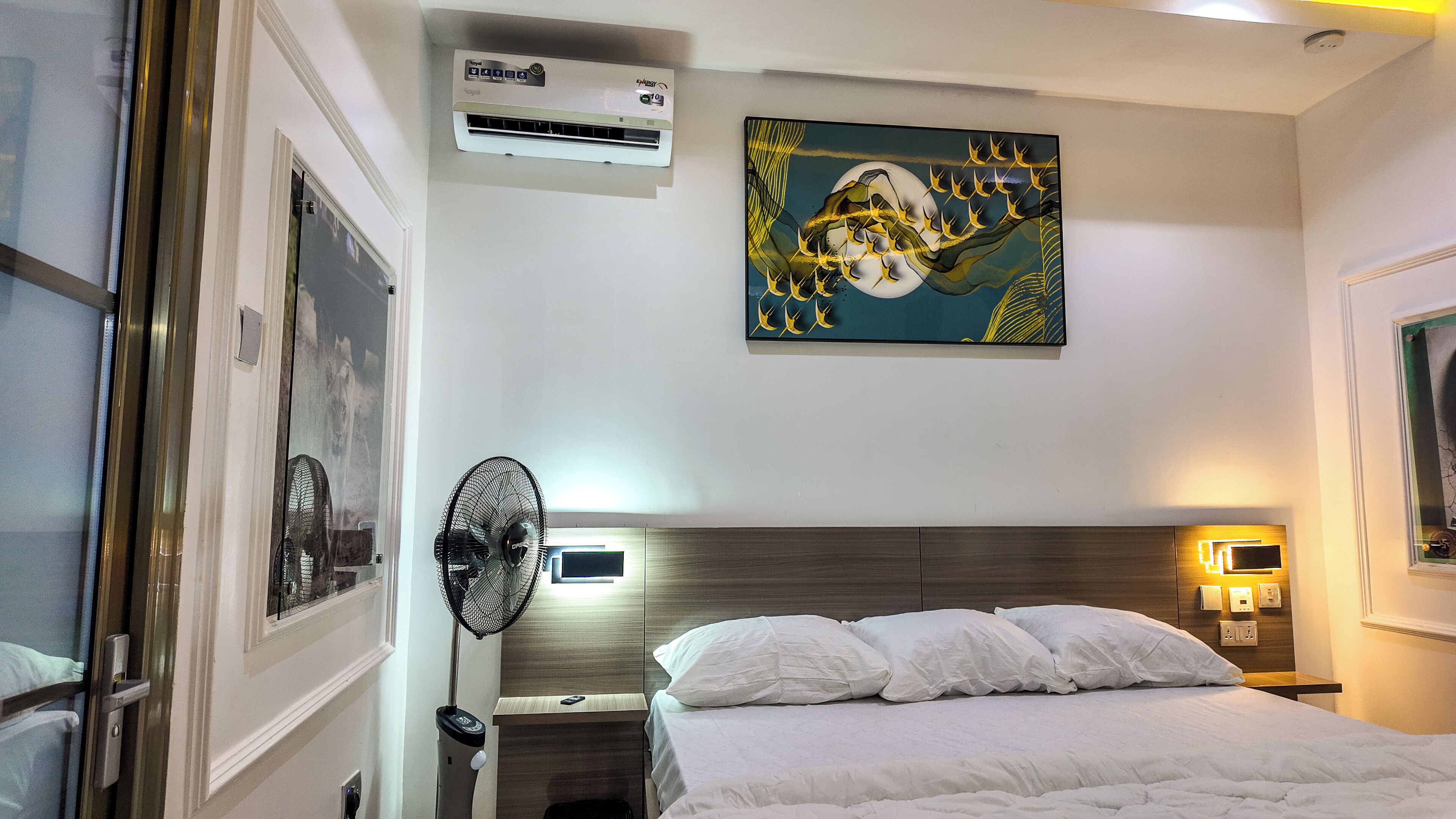 Quarto de hotel com cama, ar condicionado na parede, ventoinha no teto e um quadro.