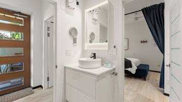 A modern bathroom with a white sink, mirror, and towel rack. There is a shower area visible through the door.