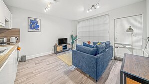 A modern living room with a sofa, a TV, and a kitchen area with a kettle. - College Lane Apartment, Bury St Edmunds (Bury St Edmunds)