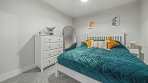 A bedroom with a white dresser, a bed with teal bedding, and a nightstand with a lamp. - College Lane Apartment, Bury St Edmunds (Bury St Edmunds)