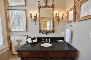 Une salle de bain avec un lavabo en granit foncé, deux robinets, un grand miroir décoratif et des appliques murales.