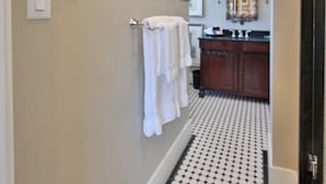 Un pasillo con suelo de baldosas blanco y negro, un mueble de madera con espejo y cuadros enmarcados en la pared.