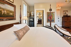 Une chambre d’hôtel avec un grand lit, un bureau, une chaise, une lampe, une commode et un tableau au mur.