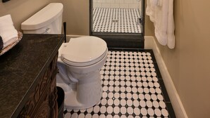 Un baño con inodoro, lavamanos y ducha. Hay cuadros enmarcados en la pared.