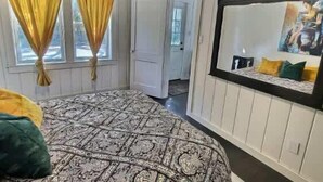 Une chambre à coucher avec une couvre-lit à motifs, un grand miroir et une porte donnant sur une autre pièce.