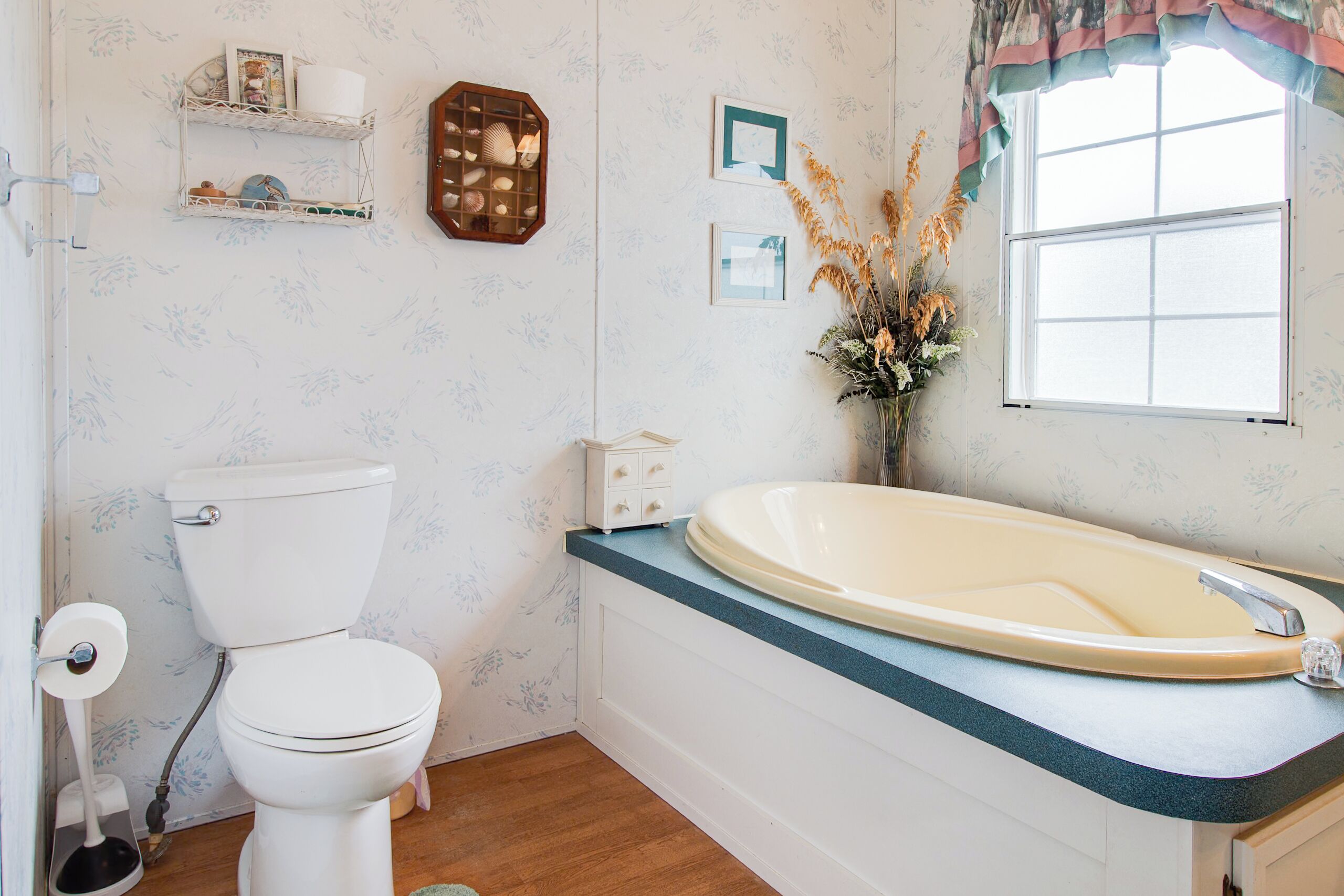 A bathroom with a toilet, a bathtub, a window, and a shelf with toiletries.