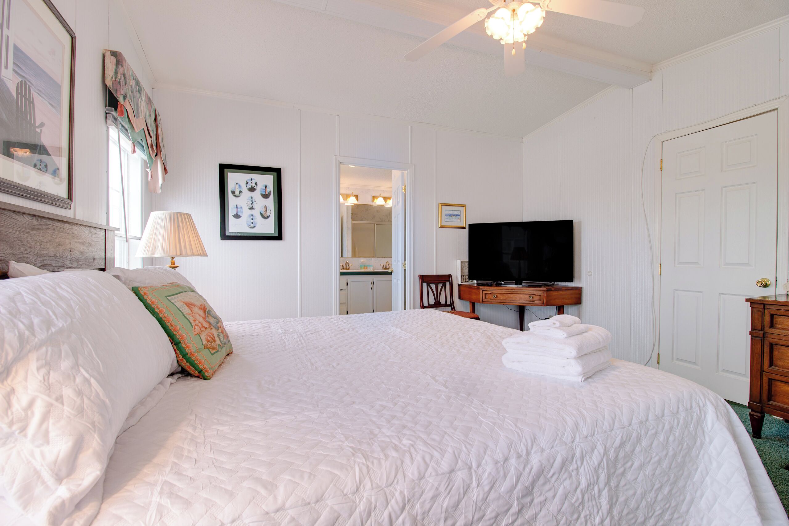 A neatly made bed with a quilted cover, a television on a wooden stand, and a door in the background.