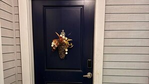 A dark blue door with a number '4' above it, a doormat with the word 'HOWDY', and a decorative wreath on the door. - Wild Western Property (Huntsville)
