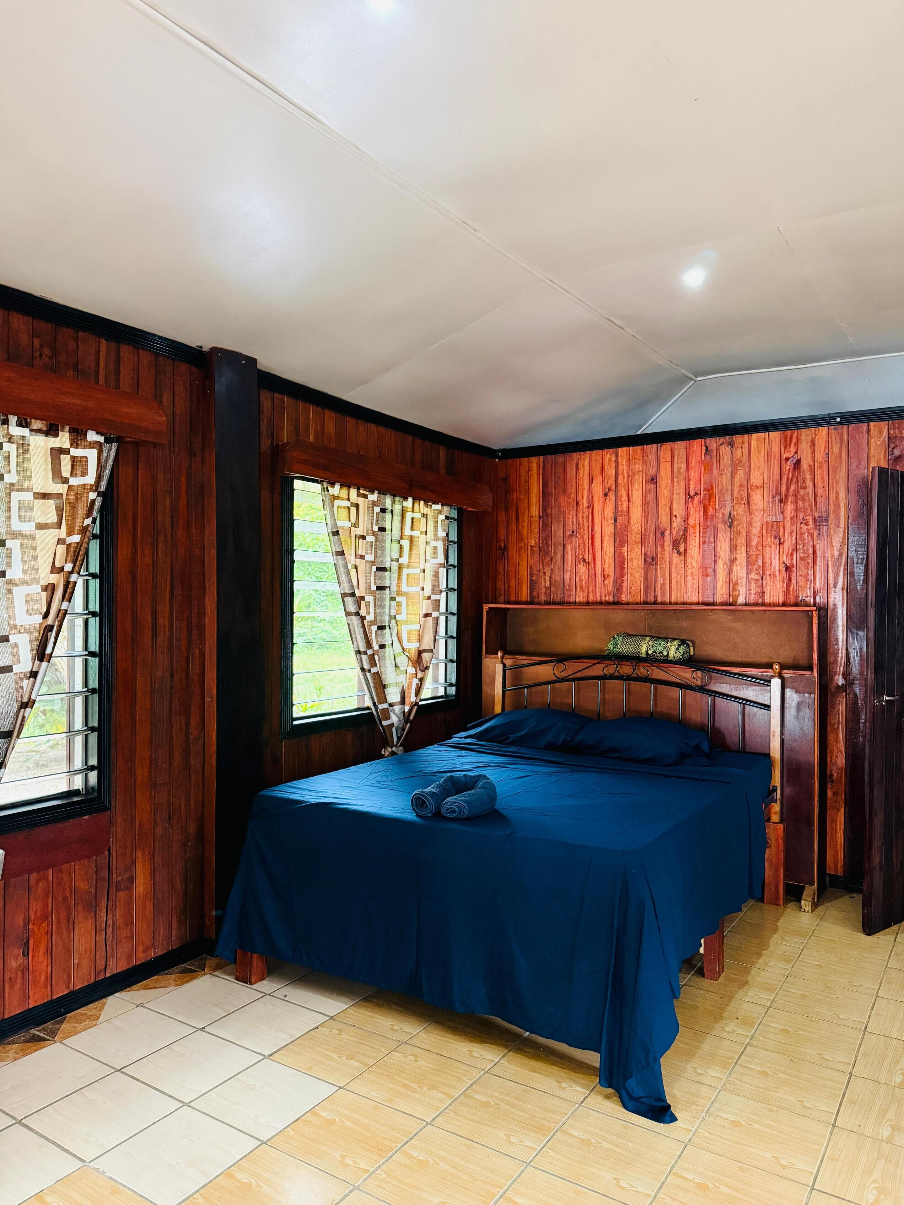 Une pièce avec un lit, des murs en bois et une fenêtre ornée de rideaux à motifs.