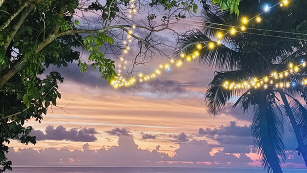Escena de playa con luces colgantes, dos sillas y un banco de madera.