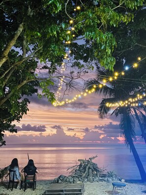 Une scène de plage avec des guirlandes lumineuses, deux chaises et un banc en bois.