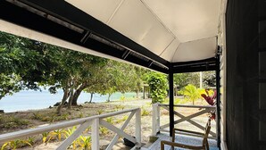 Un espacio al aire libre techado con mesa y sillas, vistas a la playa y una barandilla.