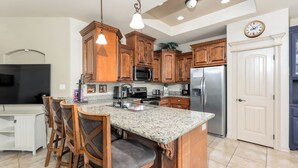 Una cocina con armarios de madera, encimeras de granito, un refrigerador de acero inoxidable e isla integrada con taburetes de bar.
