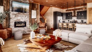 Un accogliente soggiorno con camino in pietra, una grande TV e un'area pranzo con pensili in legno, con una cucina sullo sfondo.