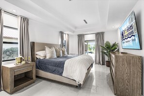 Quarto moderno com uma cama grande, uma mesa de cabeceira de madeira, uma televisão e vista para o exterior.