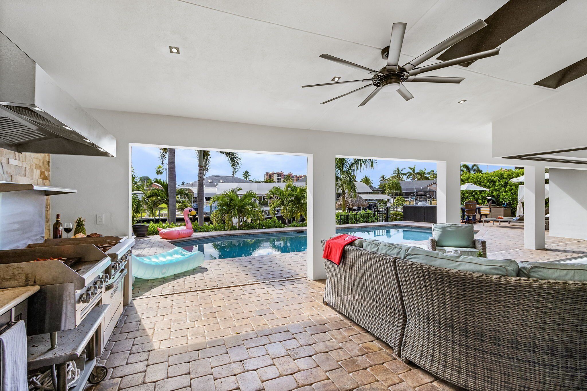 A modern kitchen with a built-in grill, a large dining area with a view of a swimming pool, and a ceiling fan.