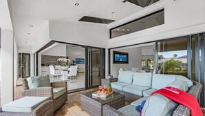 A spacious outdoor living area with wicker furniture, a glass dining table, and a large TV screen. - Sunshine, Serenity & a Heated Pool Escape for All-Day Fun – Modern Vibes Villa - Roelens (Cape Coral)