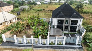 Une maison moderne à deux étages, avec un toit noir, entourée d’une végétation luxuriante et de bananiers.