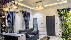 Un salon moderne avec un canapé, une table basse et un ventilateur. On y trouve des rideaux, une porte et une plante.