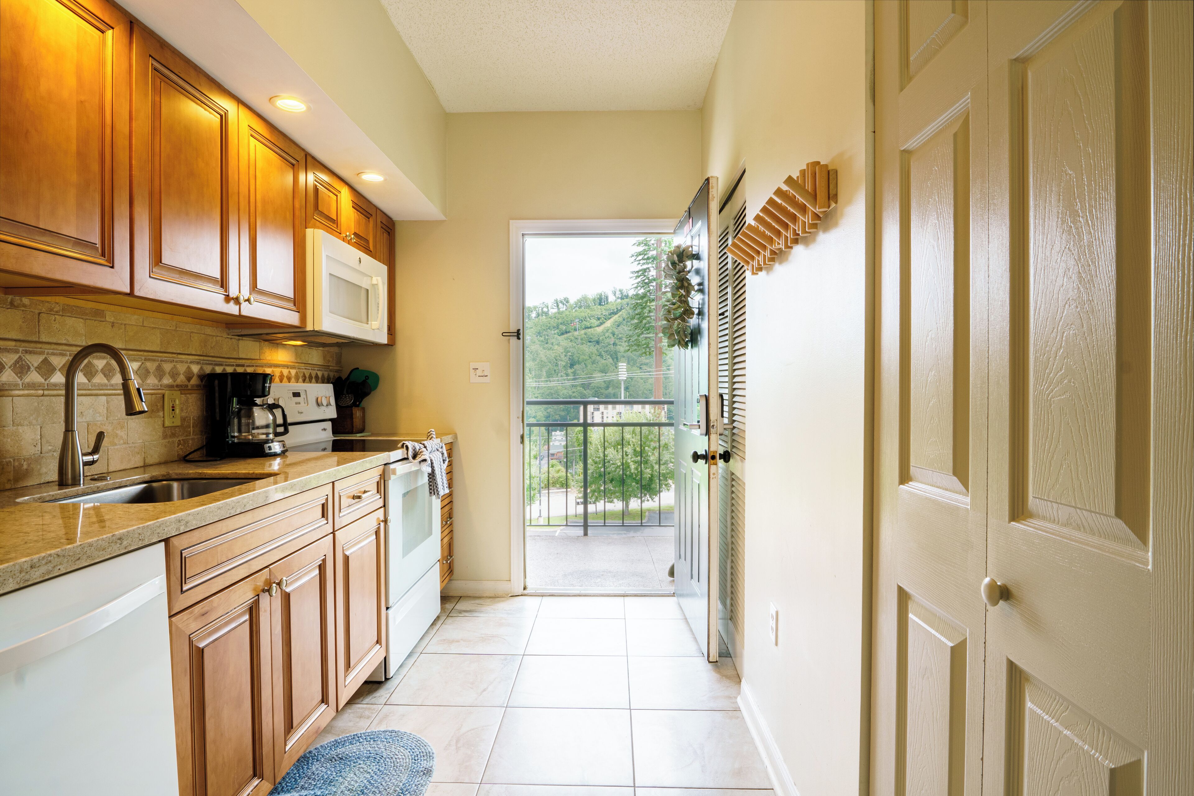 A kitchen with wooden cabinets, a microwave, and a view of a balcony.