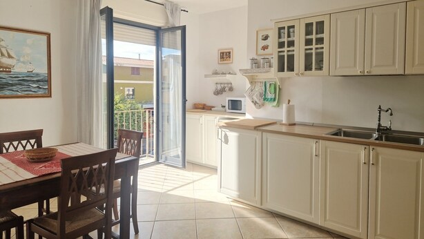 Una cocina con armarios blancos, una mesa de comedor con sillas y vistas al exterior a través de un ventanal.
