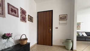 Un pasillo con una puerta de madera, un armario negro con un jarrón de flores y una cesta tejida.