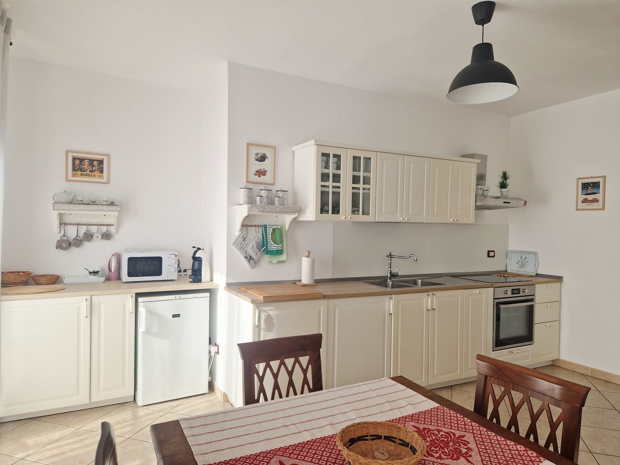 A compact kitchen with white cabinets, a microwave, a toaster, and a sink. There is a dining table with chairs and a red patterned table runner.