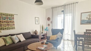 Una sala de estar con sofá, mesa de centro, sillón, mesa de comedor y ventana con cortinas.