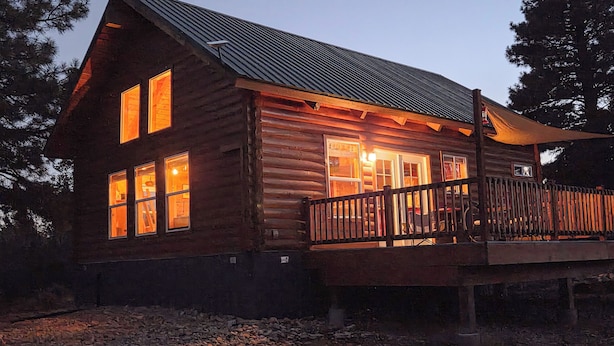 Une cabane en rondins dotée d’une terrasse en bois et de nombreuses fenêtres, entourée d’arbres.