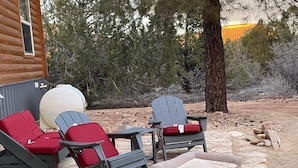 Deux fauteuils Adirondack avec des coussins rouges, un foyer en pierre et une terrasse en pierre.