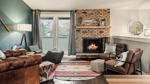 A living room with a brick fireplace, leather sofas, and a large window. - Family Arcade Retreat + Fire Pit + 4BR Near RMNP (Loveland)