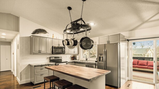A modern kitchen with a central island, bar stools, hanging pots, and a sliding glass door to a patio. - Family Arcade Retreat + Fire Pit + 4BR Near RMNP (Loveland)