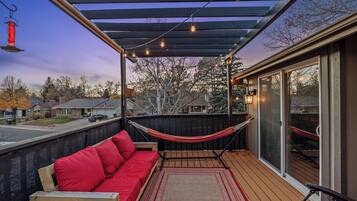 A covered outdoor deck with a red sofa, a hammock, and string lights.