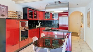 A modern kitchen with red cabinetry, a glass dining table, and a stainless steel range hood. - Center Communal D1 by Interhome (Laax)