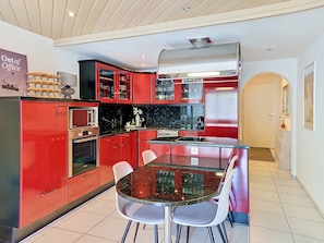A modern kitchen with red cabinetry, a glass dining table, and a stainless steel range hood.