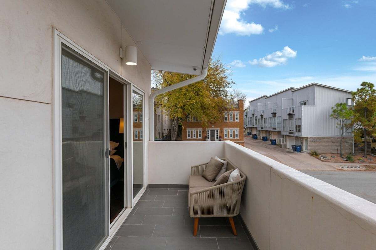 Un balcon doté d’une porte-fenêtre coulissante, d’un fauteuil en osier et offrant une vue sur les immeubles voisins.