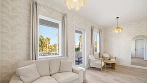 Uma sala de estar moderna com sofá, mesa de jantar e cadeiras, e janelas grandes com cortinas.