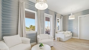 Un salon moderne avec deux canapés blancs, une table basse ronde et une vue sur l’extérieur grâce à de grandes fenêtres.
